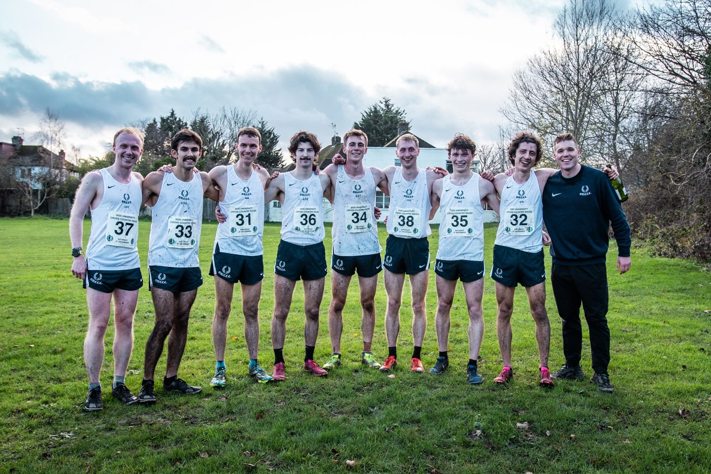 The Oxford Gentlemen’s team in race vests line up on the grass with their coach.